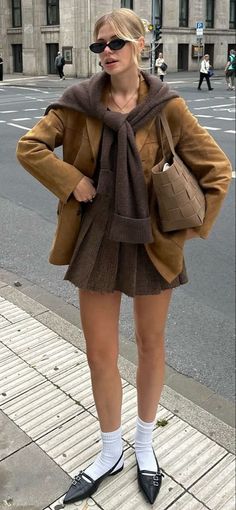 Woman in a brown jacket and pleated skirt on a city street