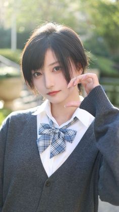 Person in a school uniform with a plaid bow and grey cardigan outdoors