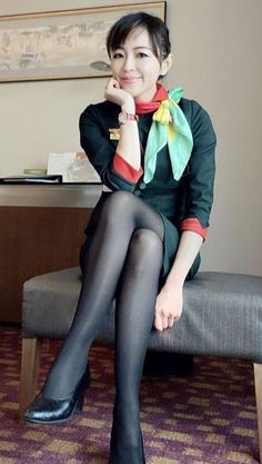 Woman in a dark uniform with a colorful scarf and black pantyhose, sitting indoors