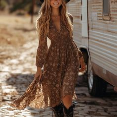 Woman in a floral dress and cowboy boots walking outdoors with a camper
