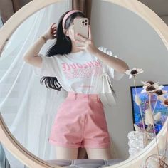 Woman taking a mirror selfie in a white t-shirt and pink shorts