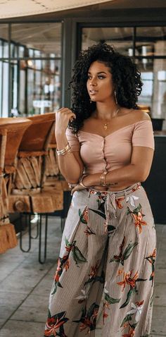 Woman with curly hair wearing an off-shoulder top and floral pants indoors
