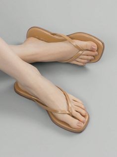 Feet wearing tan flip flops with clear nail polish on a gray background