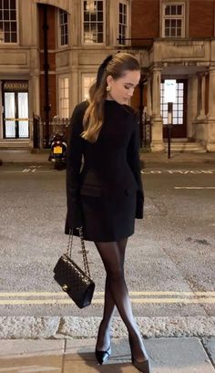 Woman in a black dress and high heels standing on a street at night
