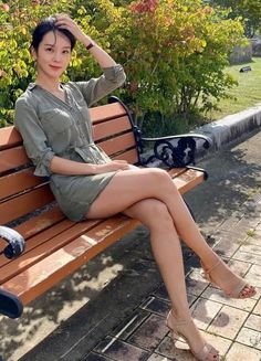 Woman in a short green dress sitting on a park bench with crossed legs