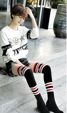 Person with short hair wearing a white sweatshirt and thigh-high socks, sitting outdoors