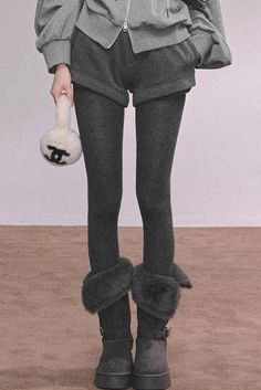 Person in a gray hoodie, shorts, and dark leggings holding a small bag