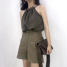 Woman in a dark green halter top and shorts holding a shoulder bag