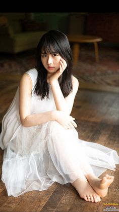 Woman in a white dress sitting on a wooden floor with bare feet