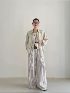 Woman in striped pants and an oversized shirt holding a coffee cup indoors
