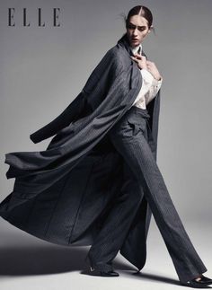 Woman in a pinstripe suit and long coat in a studio setting