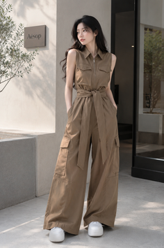 Woman in a brown jumpsuit and white sneakers standing outdoors