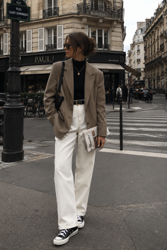 Woman in a blazer and white pants on a city street holding a newspaper