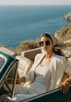 Woman in a convertible car with a head scarf and sunglasses overlooking the ocean