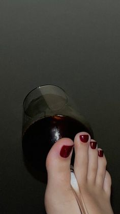 Foot with red nail polish holding a wine glass against a dark background