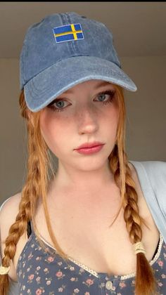 Woman with red braided hair and a baseball cap looking at the camera