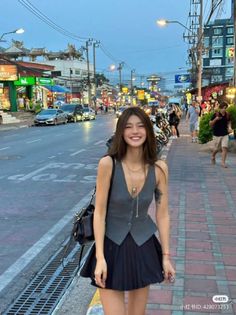 Smiling woman in a vest and pleated skirt on a city street at night