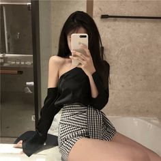 Woman in an off-shoulder top and gingham shorts taking a mirror selfie