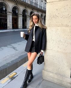 Woman in a black coat and mini skirt holding a coffee cup on a city street