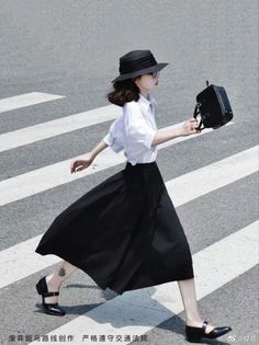Woman in a black hat and long skirt crossing a street