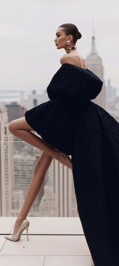 Woman in a black off-shoulder dress and high heels posing on a rooftop
