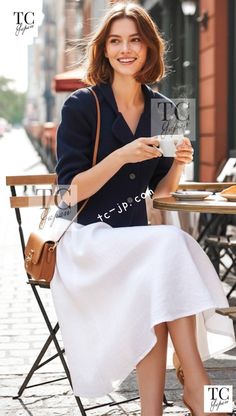 Woman with short hair in a navy jacket and white skirt at an outdoor cafe