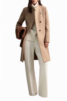 Woman in a camel coat, white turtleneck, and wide-leg pants holding a brown bag