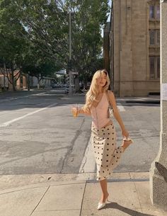 Woman with long blonde hair in a pink top and polka dot skirt on a street