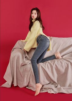 Woman in a yellow sweater and skinny jeans posing on a draped surface
