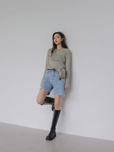 Woman in denim shorts and knee-high boots leaning against a white wall