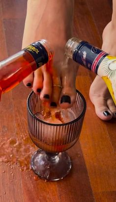 Feet pouring Aperol and prosecco into a glass, spilling on a wooden floor