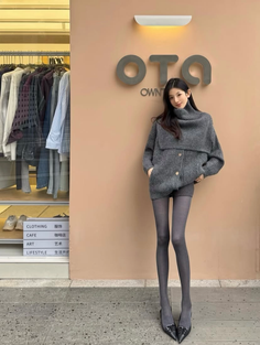 Woman in a gray sweater and tights standing outside a store