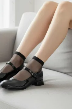 Person wearing black mary jane shoes and sheer socks while sitting indoors