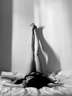 Woman lying on a bed with legs up against a wall, a book nearby