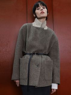 Woman with short hair wearing a belted herringbone coat against a red background