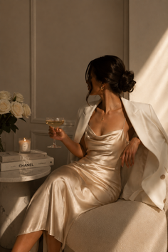 Woman in a satin dress and white blazer holding a champagne glass indoors
