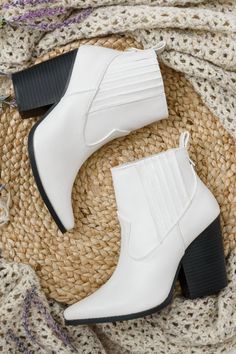 Pair of white ankle boots with chunky heels on a braided rug with a knitted blanket