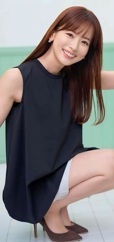 Woman in a black top and white shorts squatting and smiling indoors