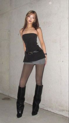Woman in a black tube top, mini skirt, and black boots posing indoors