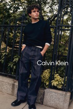 Man with curly hair wearing a dark sweatshirt and wide leg jeans outdoors