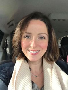 Woman with short brown hair and a scarf smiling in a car