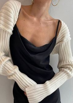Woman wearing a black slip dress and a white knit shrug with gold hoop earrings