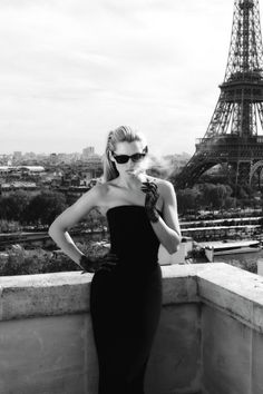 Woman in a strapless dress and sunglasses smoking on a rooftop with the Eiffel Tower