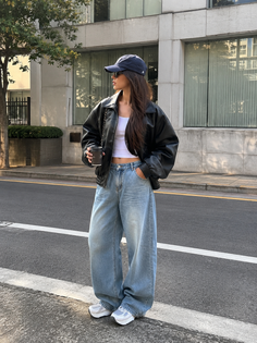 Woman in a baseball cap, leather jacket, and baggy jeans on a street