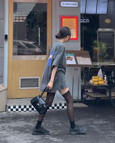 Woman in a t-shirt dress and black stockings walking past a burger restaurant
