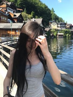 Woman with long dark hair in a grey tank top by a lake in a village