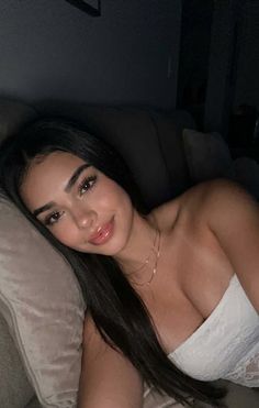 Woman with long black hair wearing a white tube top and gold necklace, lying down