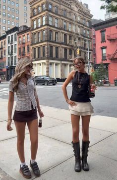 Two young women standing on a city sidewalk with buildings in the background