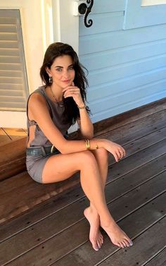 Woman with long dark hair in a gray dress sitting on a wooden floor