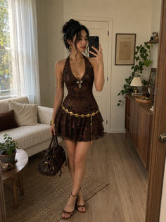 Woman in a brown halter dress and gold jewelry taking a mirror selfie indoors